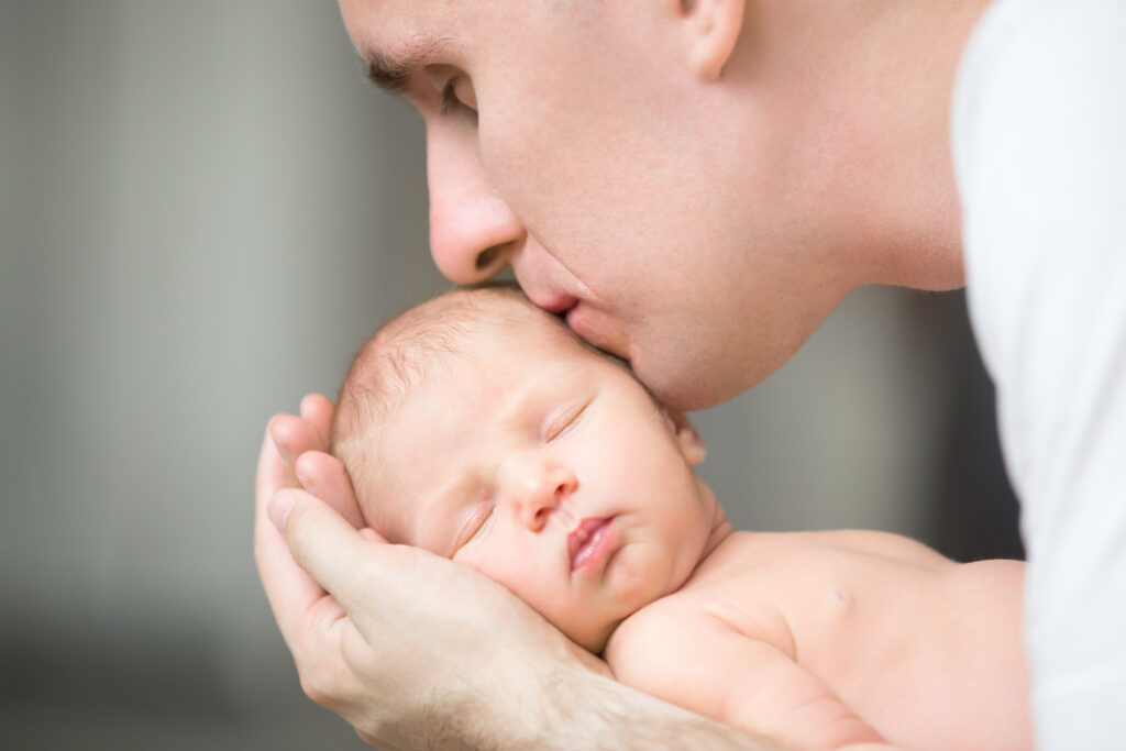 Father kissing a newborn baby, representing the start of paternity leave in Malaysia.